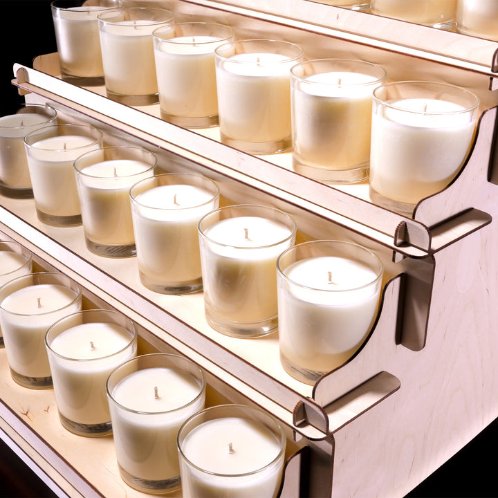 Row of white candles in glass holders on a wooden display shelf